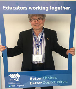 male professor holding sign that reads 'educators working together'